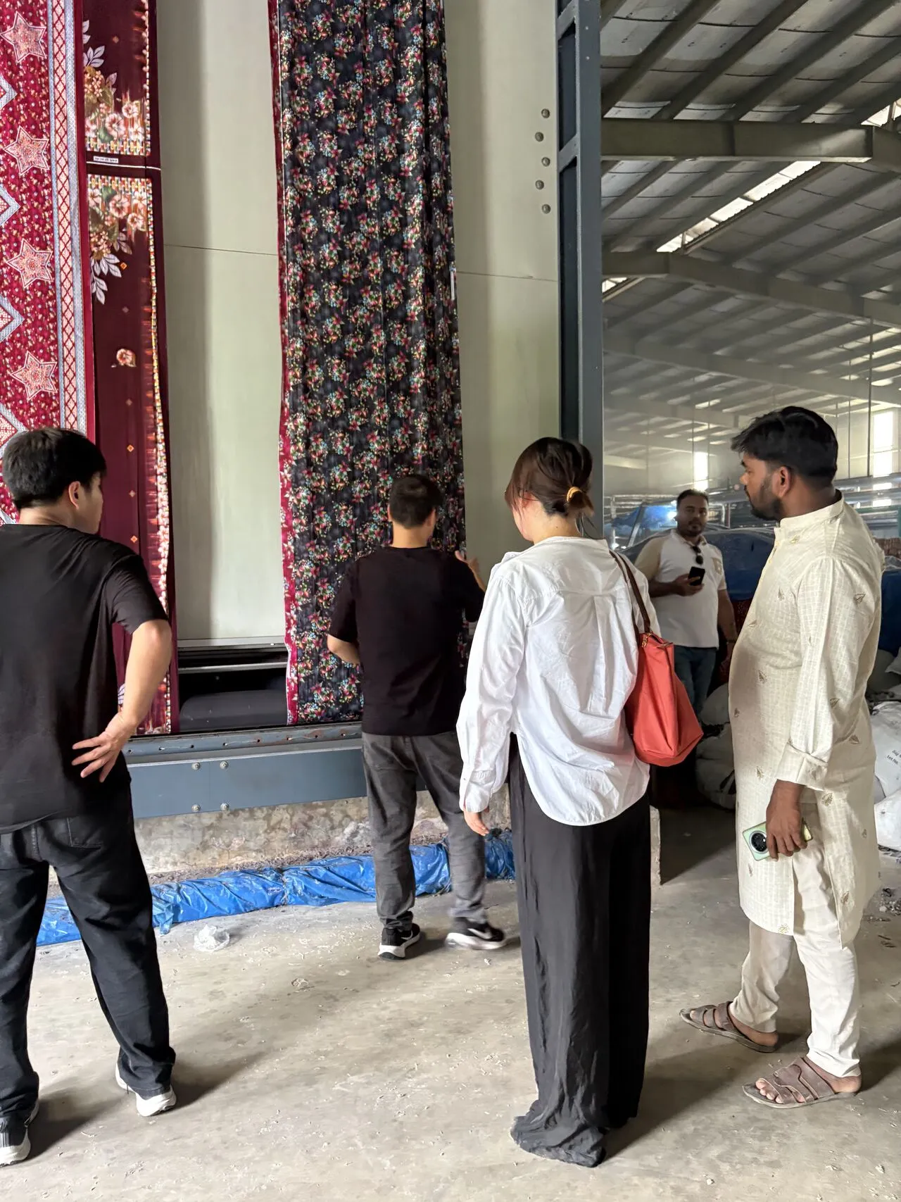 Visitors examining hanging printed fabrics inside a textile factory