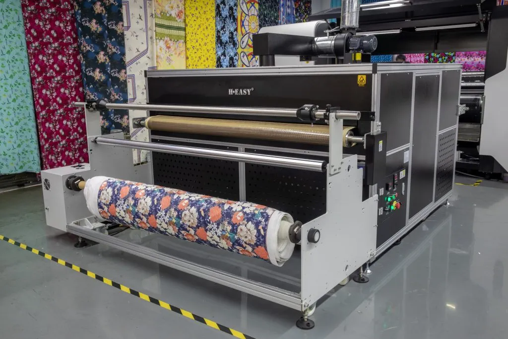 A roll-to-roll digital textile printer laying down color across fabric moving over the platen