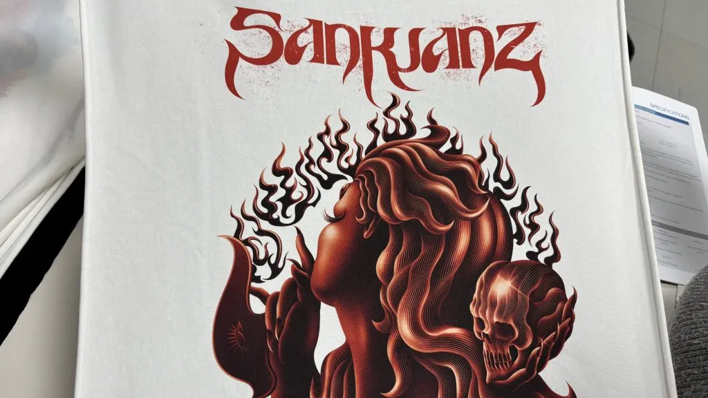 Camiseta branca estampada com uma figura ilustrada em vermelho e preto e letras estilizadas