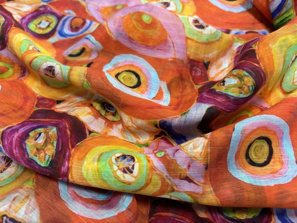 Tejido estampado naranja con grandes motivos circulares multicolores plegado en ondas suaves