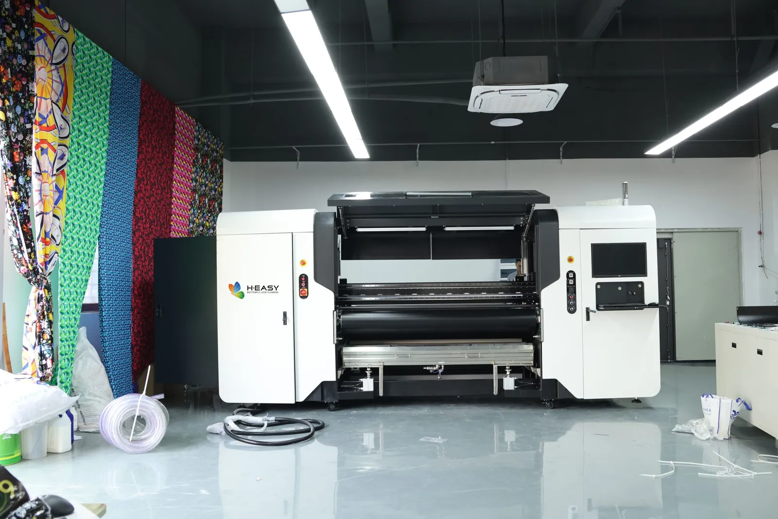 Impresora textil de bobina a bobina en un taller junto a muestras de tejido estampado colgadas