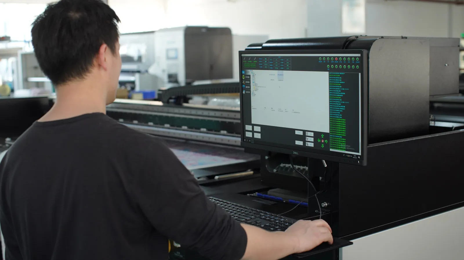 Operario revisando el software de control de impresión junto a una impresora textil de gran formato