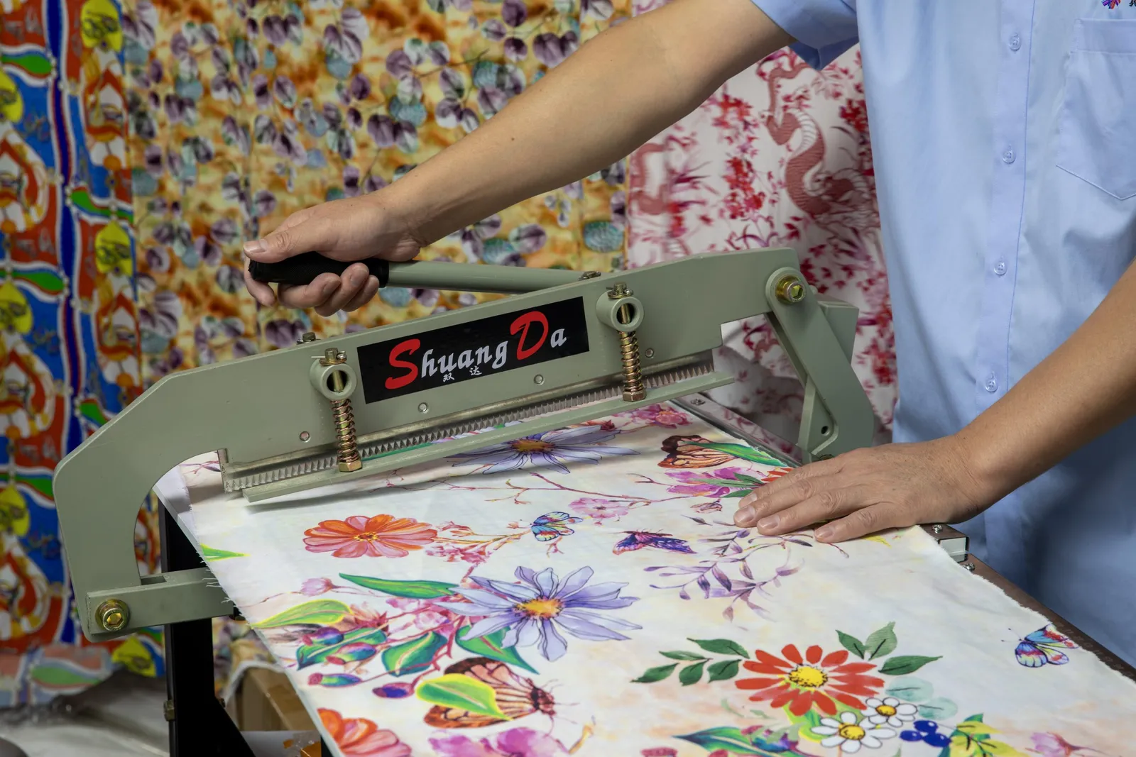 Operario cerrando una prensa térmica plana sobre tejido estampado con motivos florales