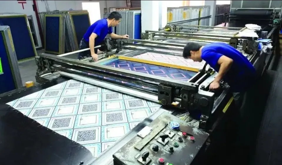 Dos operarios alineando pantallas grandes sobre tejido estampado en una mesa serigráfica industrial