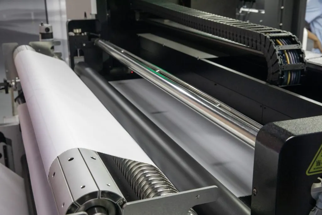 White textile roll feeding across metal guide and tension rollers inside a printer