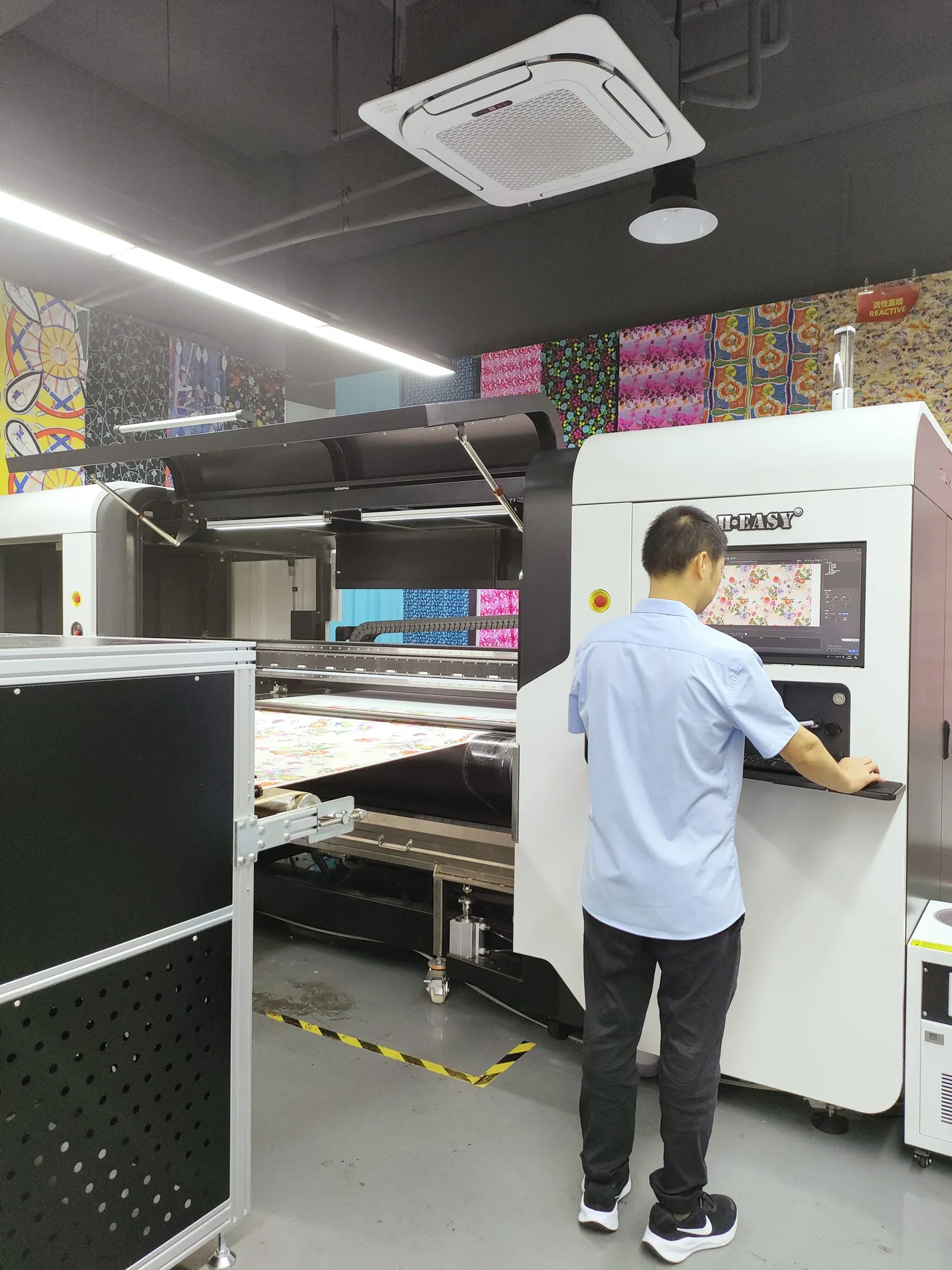 Operario usando la consola de control junto a una impresora textil de bobina a bobina en un showroom de tejidos