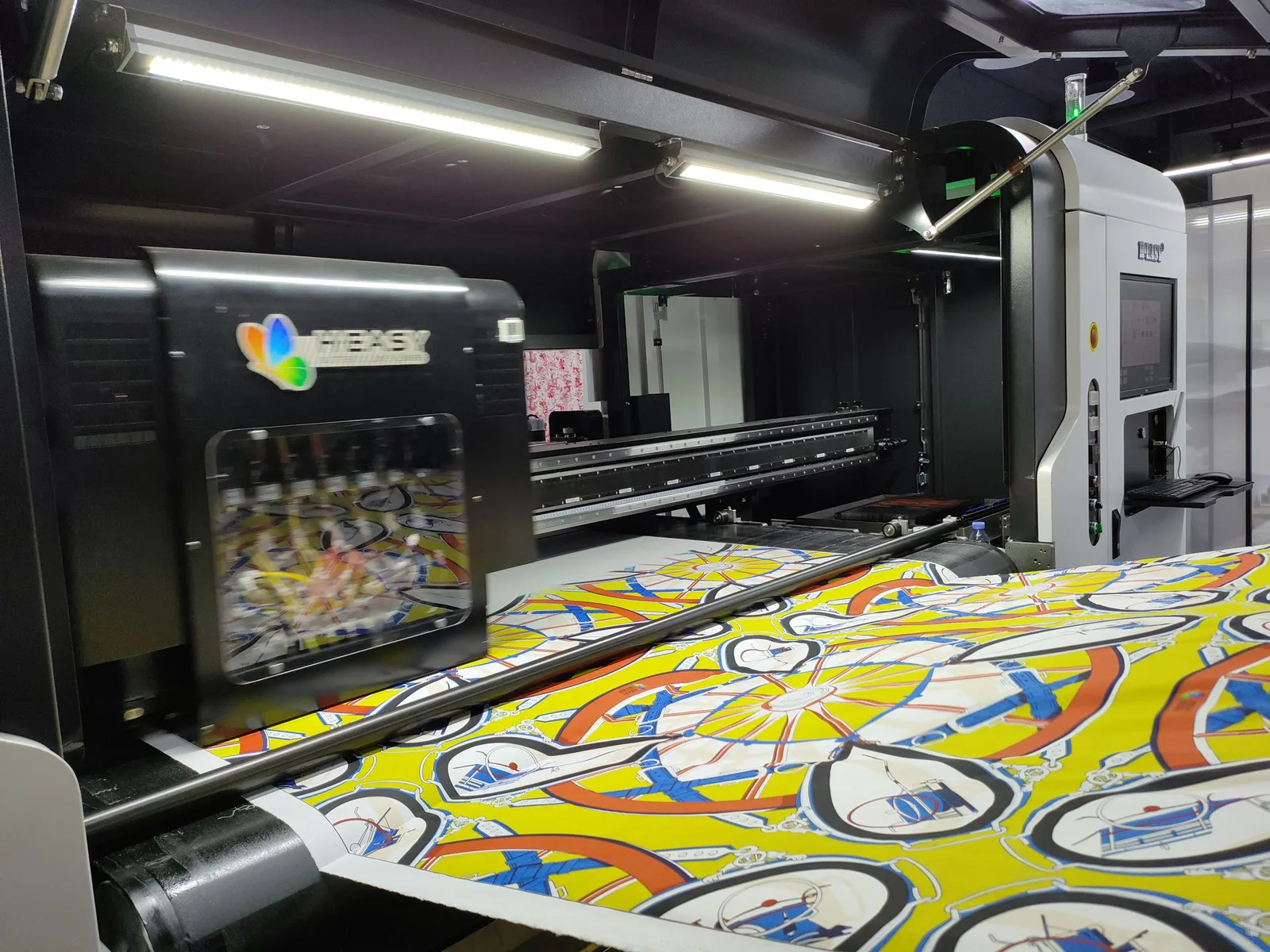 Carro de impresión desplazándose sobre un tejido de estampado vivo en una línea textil industrial