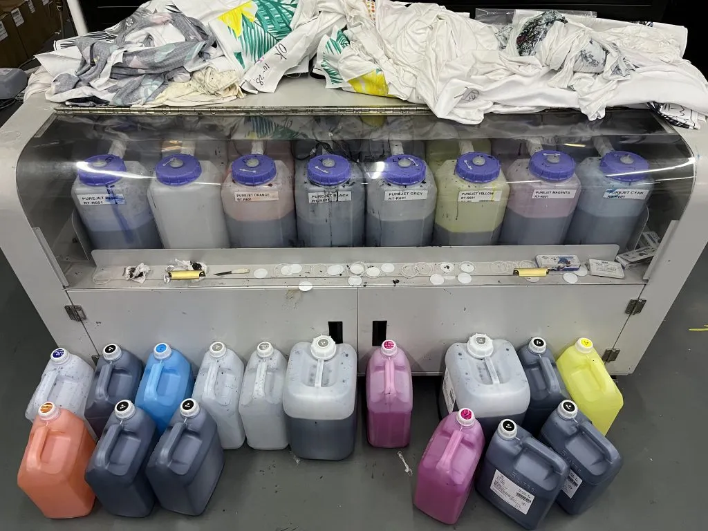 Envases de tinta textil a granel colocados delante de los depósitos de alimentación etiquetados de una impresora
